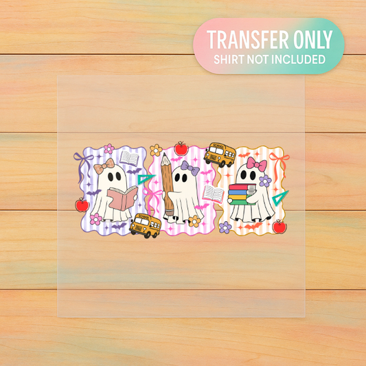 Cartoon ghost characters with school-themed items on a clear transfer sheet, placed on a wooden surface.